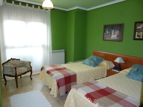 A room with two beds, a chair, a radiator, and a window with curtains. - Hostal Ciudad de Nájera (Najera)