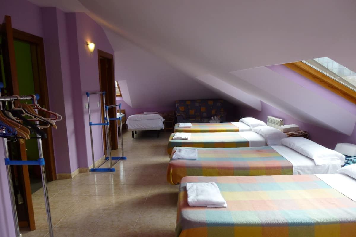 Une chambre d’hôtel avec trois lits, un étendoir et une lucarne.