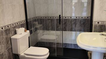 Un baño con ducha de vidrio, dos inodoros y un lavabo sobrepedal.