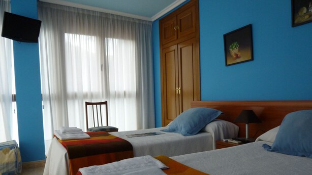 Een hotelkamer met twee bedden, een houten garderobe, een televisie en een schilderij aan de muur.