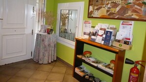Een receptiegedeelte met een groene wand, een ingelijst schilderij, een receptiebalie met brochures, een brandblusser en een deur.
