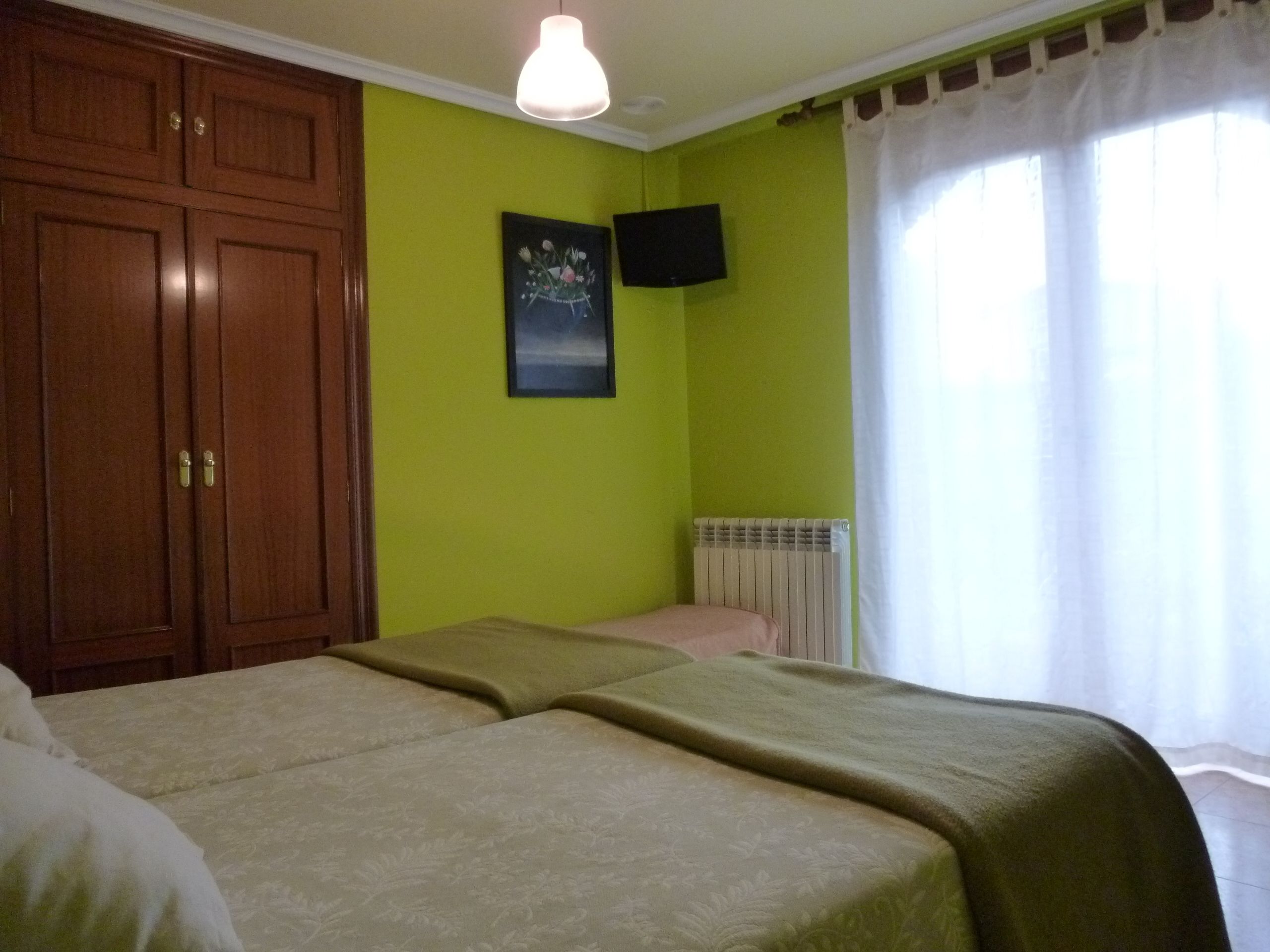 A room with two beds, a wooden wardrobe, a mounted TV, and a radiator.