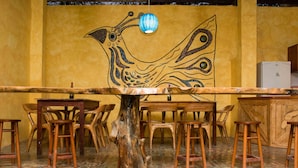A restaurant interior with wooden tables and chairs, a mural on the wall, and a unique tree stump centerpiece. - Tuzco Lodge (Puerto Lopez)