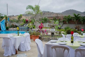 An outdoor dining area with tables set for a meal, surrounded by a pool and a waterfall. - Tuzco Lodge (Puerto Lopez)
