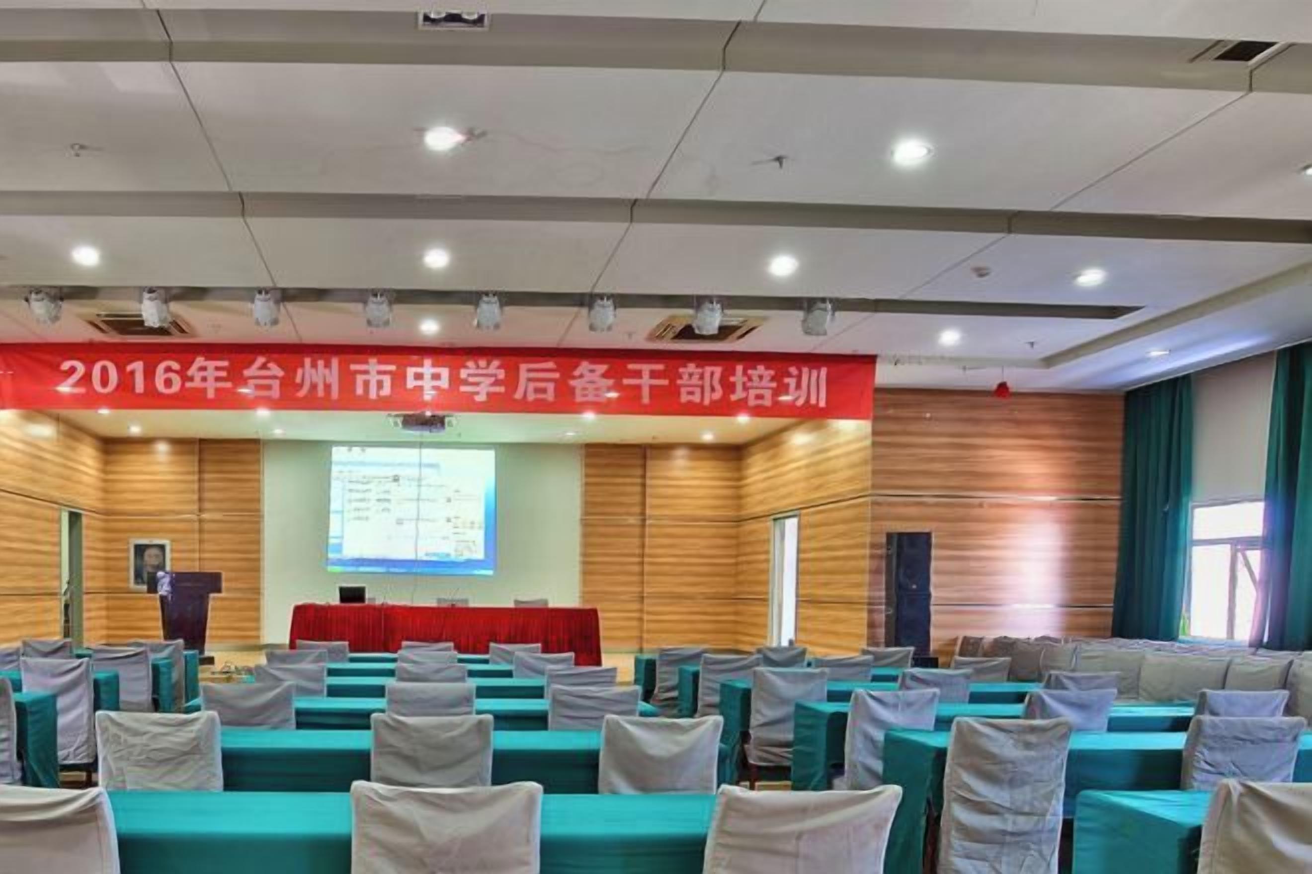 A conference room with rows of tables and chairs, a podium, and a presentation screen.