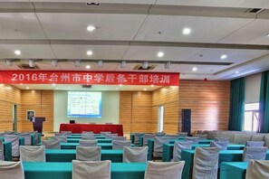 A conference room with rows of tables and chairs, a podium, and a presentation screen. - Jinjiang Inn (Linhai Chonghemen) (TAIZHOU)