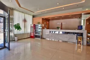 Zona de recepción de hotel con mostrador de mármol, escritorio y una planta en maceta.