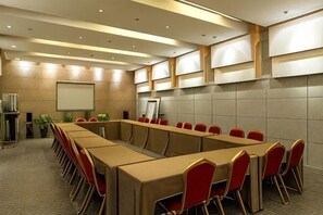 Une salle de conférence avec une longue table, des chaises rouges, un écran de projection et un tableau blanc.