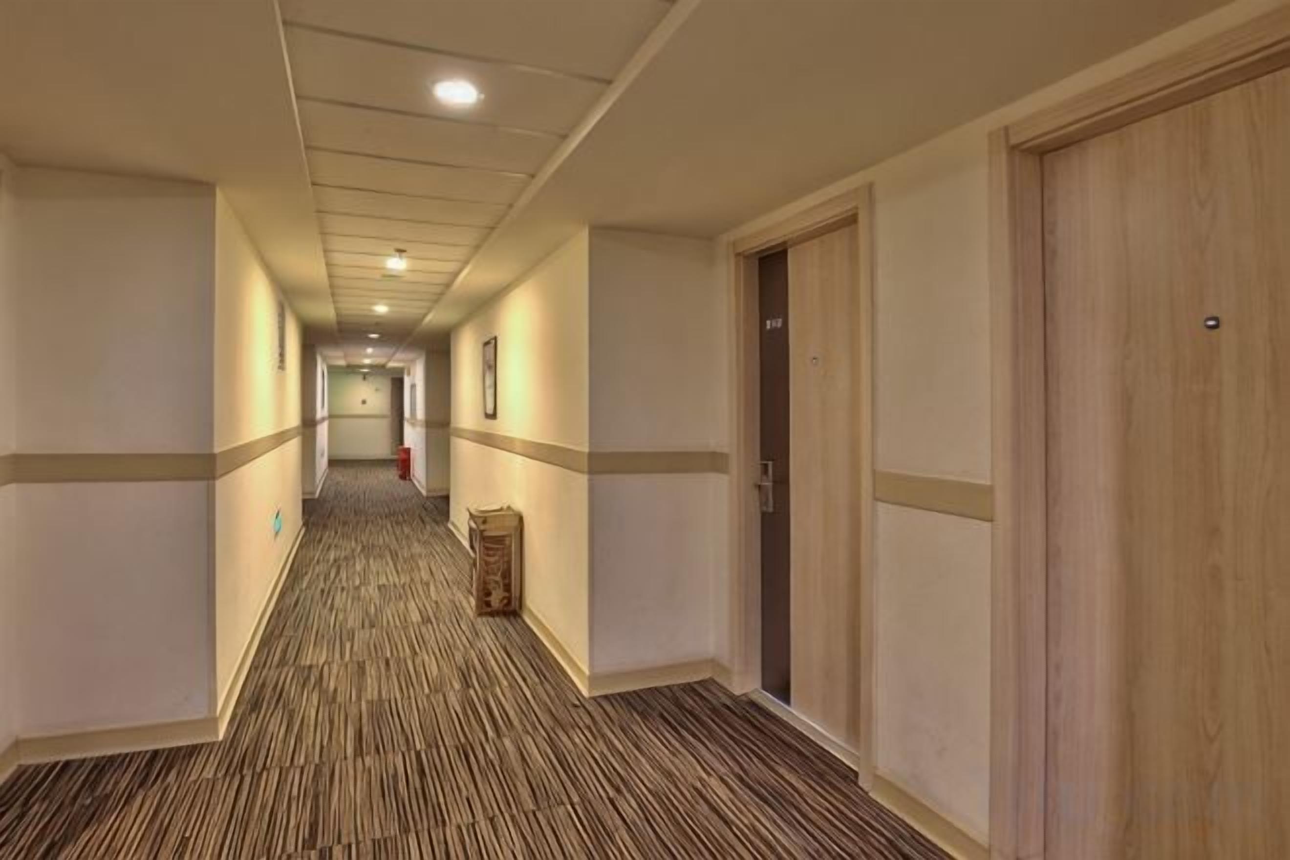 A hotel corridor with carpeted floors, wooden doors, and framed pictures on the walls.
