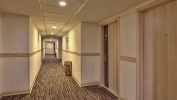 A hotel corridor with carpeted floors, wooden doors, and framed pictures on the walls.