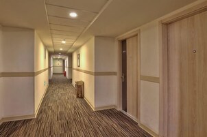 Un pasillo de hotel con pisos alfombrados, puertas de madera y cuadros en las paredes.
