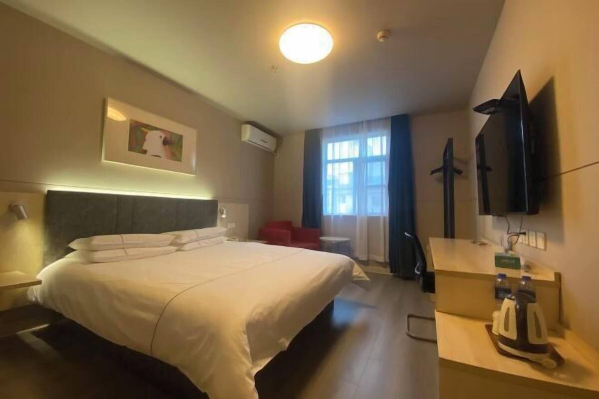 Une chambre d’hôtel avec un grand lit, un bureau avec une bouilloire, une télévision à écran plat et une fenêtre avec des rideaux.