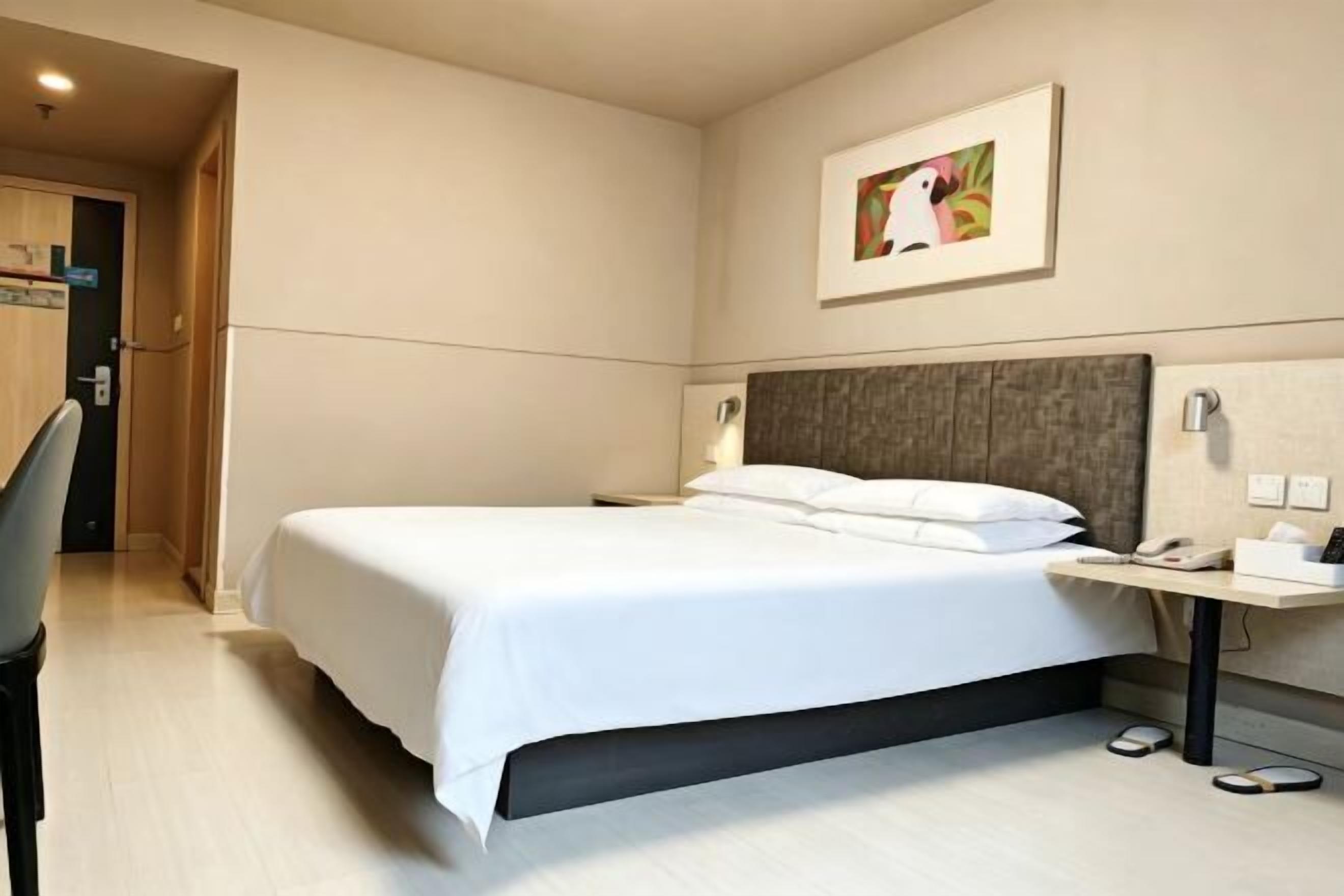 Habitación de hotel con cama, mesita de noche, lámpara y una obra de arte en la pared.