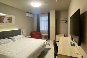 Una habitación de hotel con cama, escritorio, silla, televisor y una silla roja.