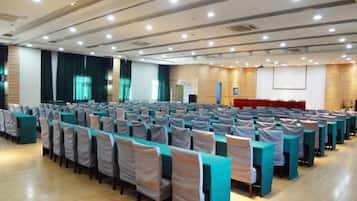 A conference room with rows of tables and chairs, a stage, and a projection screen.