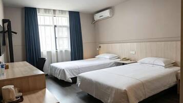 Habitación de hotel con dos camas, un escritorio, una silla, una lámpara y un ventanal con cortinas.