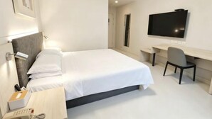 Hotellihuone, jossa on sänky, yöpöytä, lamppu, työpöytä, tuoli, televisio ja puhelin.