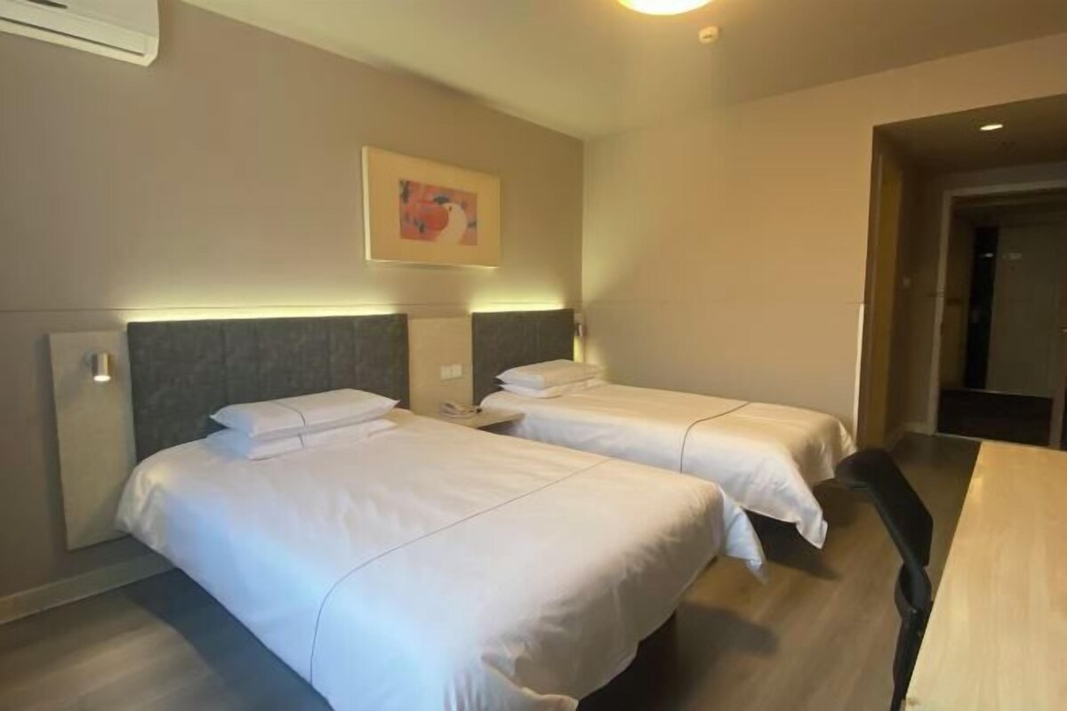 A hotel room with two single beds, a wooden desk, and a framed picture on the wall.