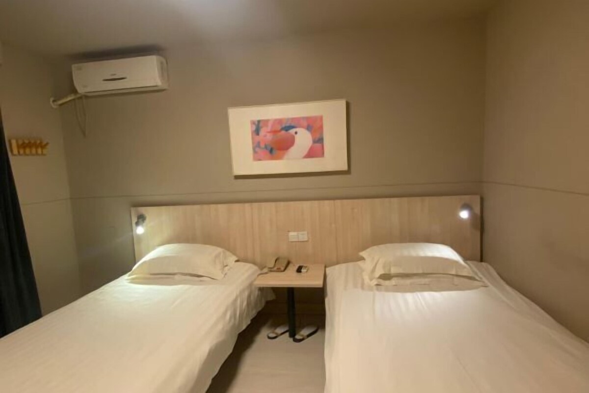 A hotel room with two single beds, a small table with a phone, and a wall-mounted air conditioner.