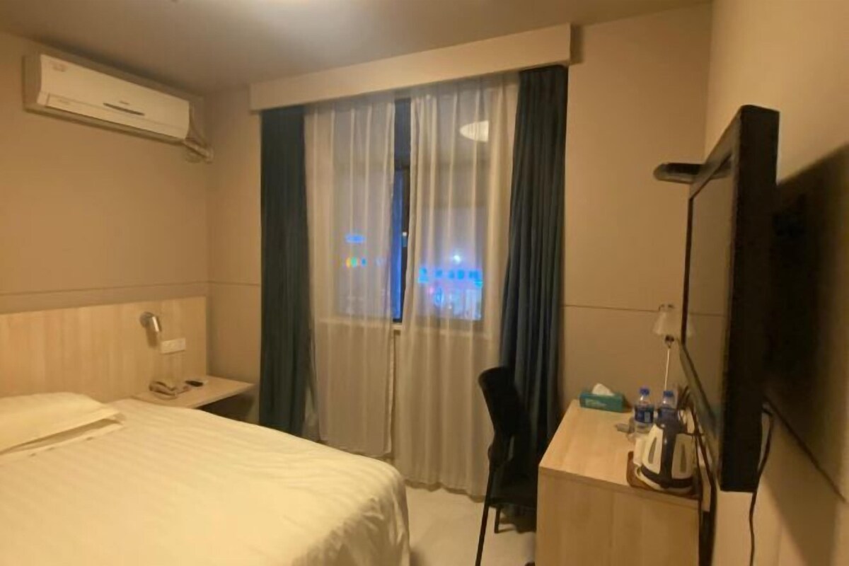 A hotel room with a bed, a desk, a chair, a TV, and a window with curtains.