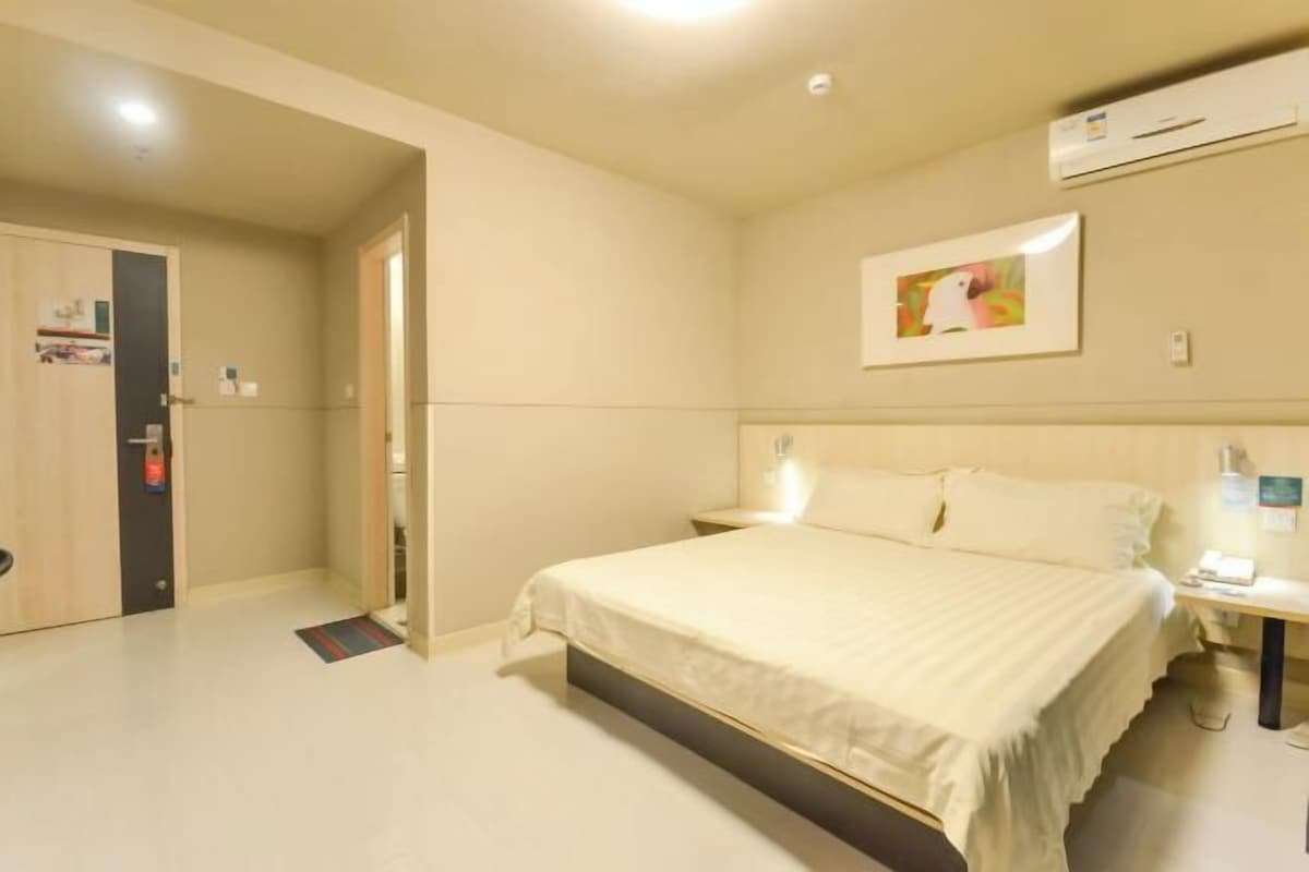 A hotel room with a bed, bedside table, and a wall-mounted air conditioner.