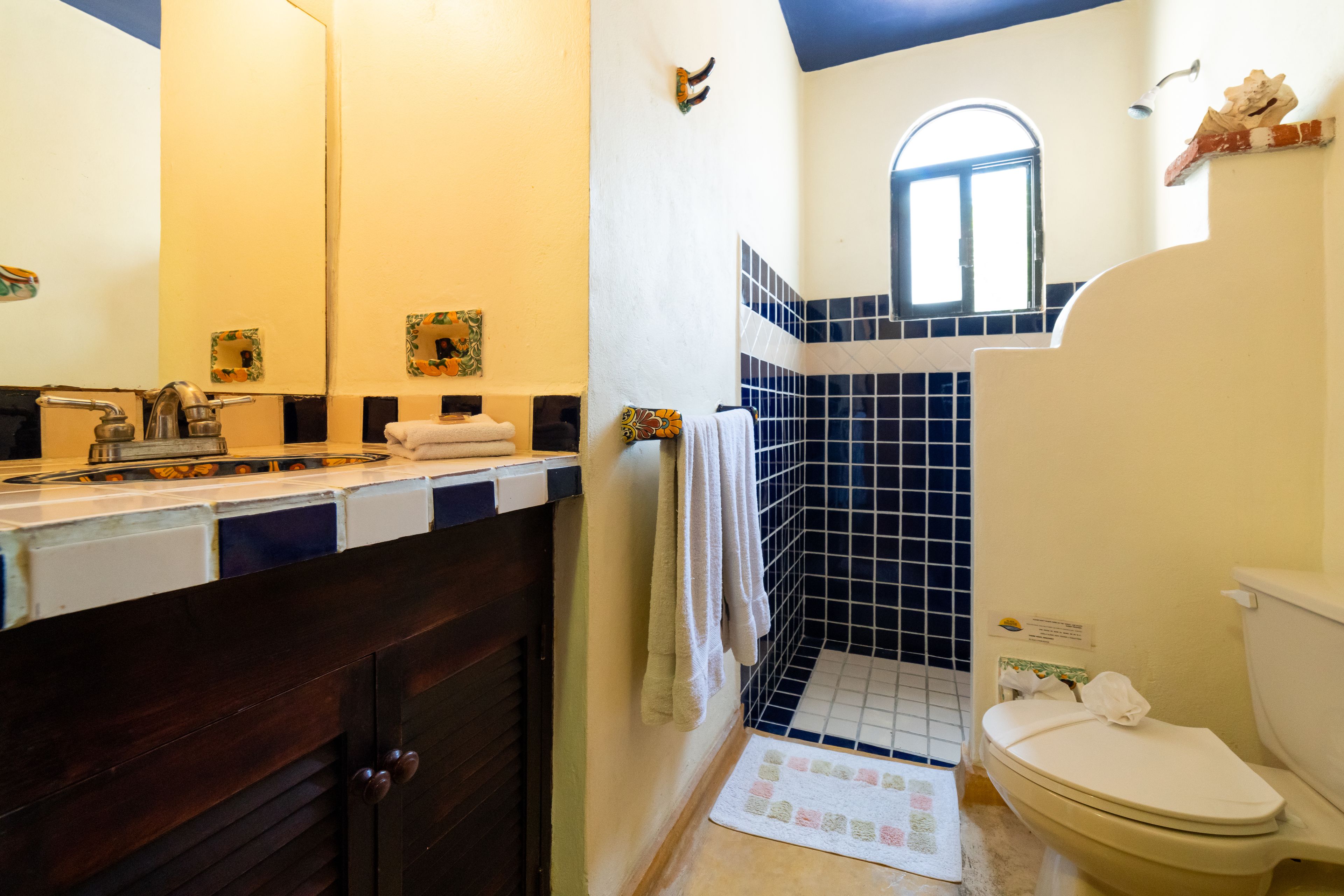 Une salle de bain avec un meuble en bois foncé, un lavabo blanc, une douche carrelée de bleu et de blanc, et des toilettes blanches.