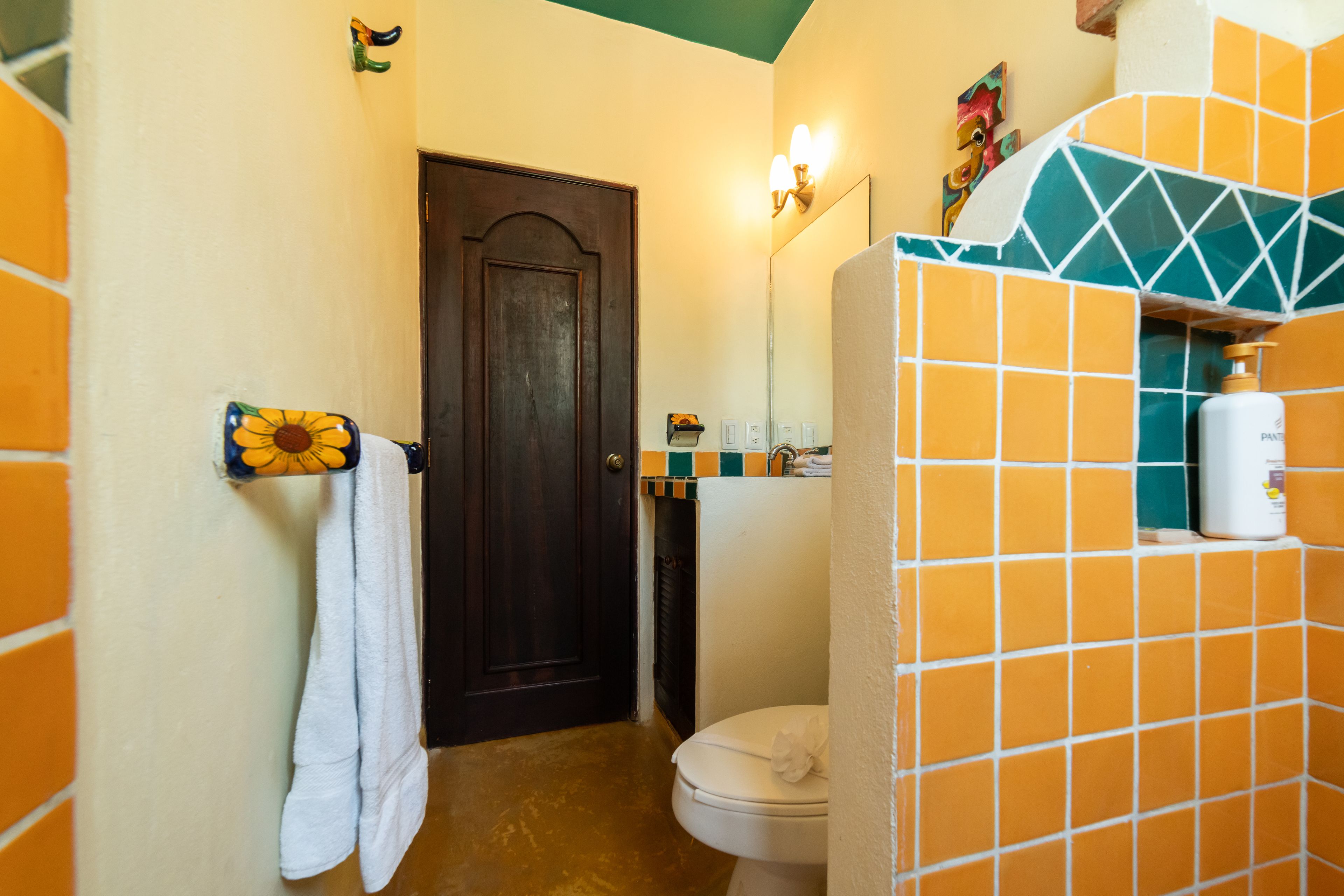 Um banheiro com vaso sanitário branco, um porta-toalhas com toalha branca, uma porta escura e uma parede revestida com padrão geométrico.