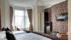 A hotel room with two beds, a TV, a wardrobe, and a view of the city. - Kildonan Guesthouse (Aberdeen)