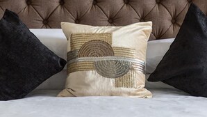 A tufted headboard with a decorative pillow and two dark pillows on a bed. - Kildonan Guesthouse (Aberdeen)