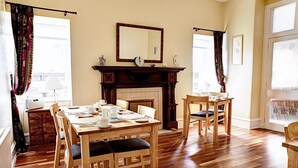 A dining room with a wooden table set for four, a fireplace, and a large mirror on the wall. - Kildonan Guesthouse (Aberdeen)