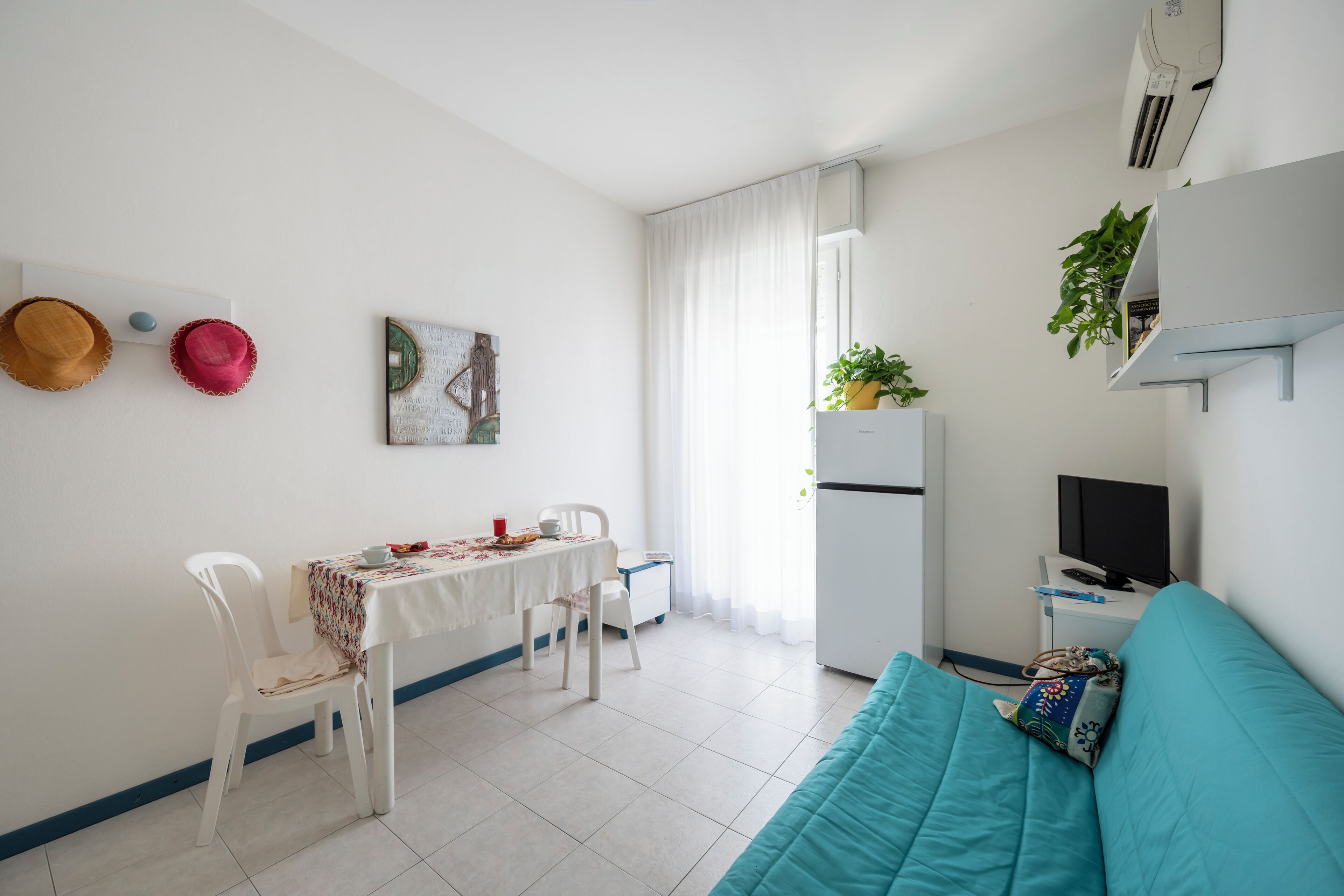 Une petite pièce propre, comprenant une table à manger, des chaises, un canapé, un téléviseur et un réfrigérateur.