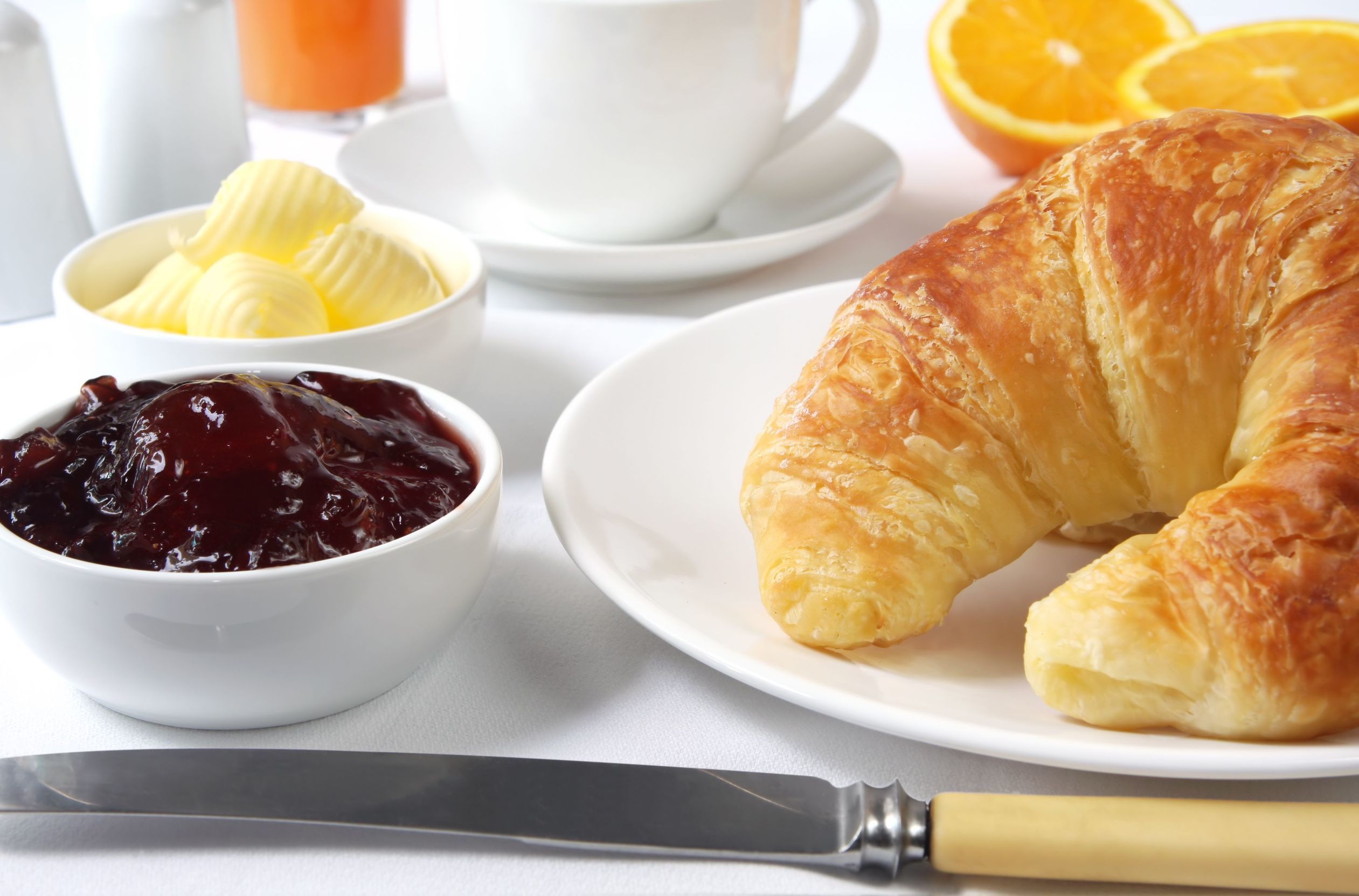Une table dressée pour le petit-déjeuner avec un croissant, du beurre, de la confiture, une orange et un verre de jus.