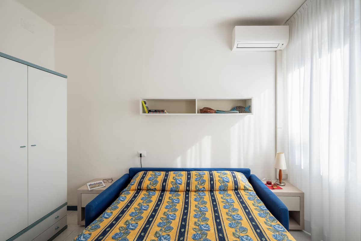 Een slaapkamer met een bed, een kledingkast, een bureau en een plank met boeken.
