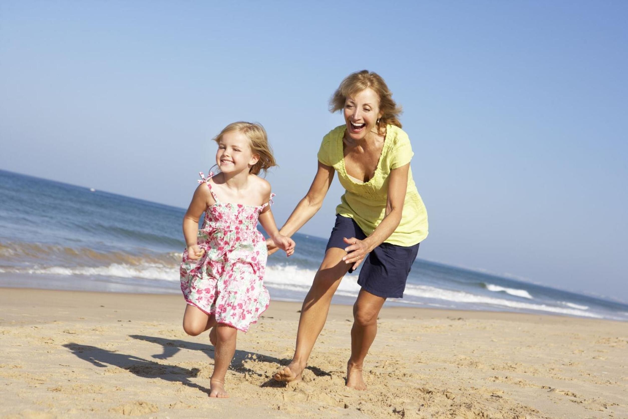 Eine Frau und ein Kind laufen auf einem sandigen Strand, im Hintergrund das Meer.