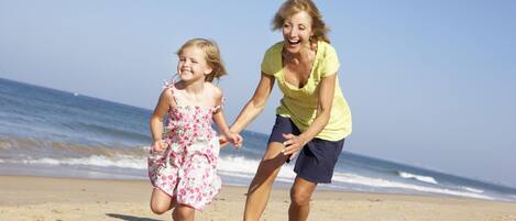 A woman and a child running on a sandy beach with the ocean in the background.