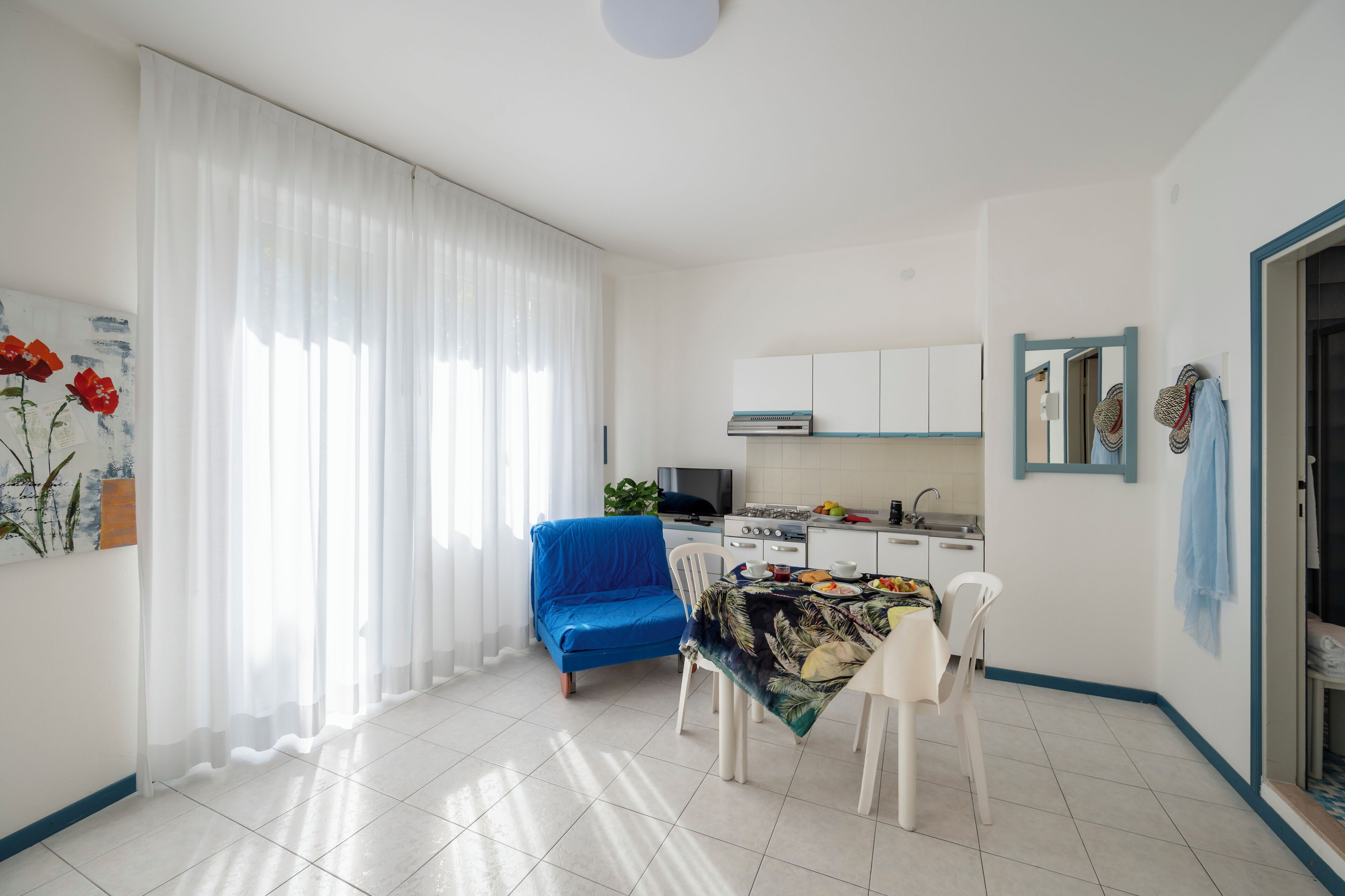 A modern kitchen with white cabinets, a blue sofa, and a dining table with a tropical print tablecloth.