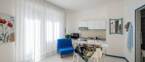 A modern kitchen with white cabinets, a blue sofa, and a dining table with a tropical print tablecloth.