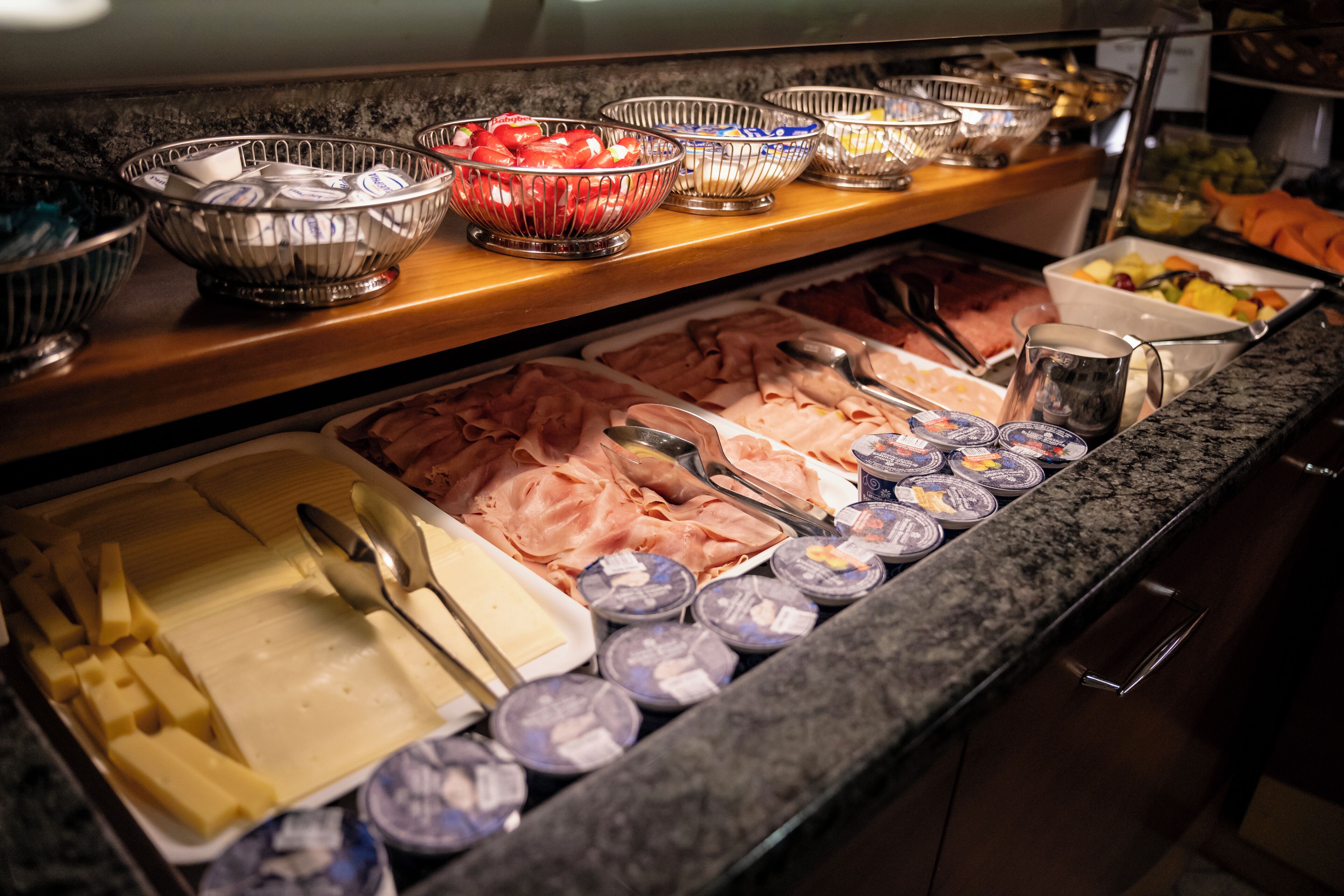 A buffet with various food items including meats, cheeses, and fruits.