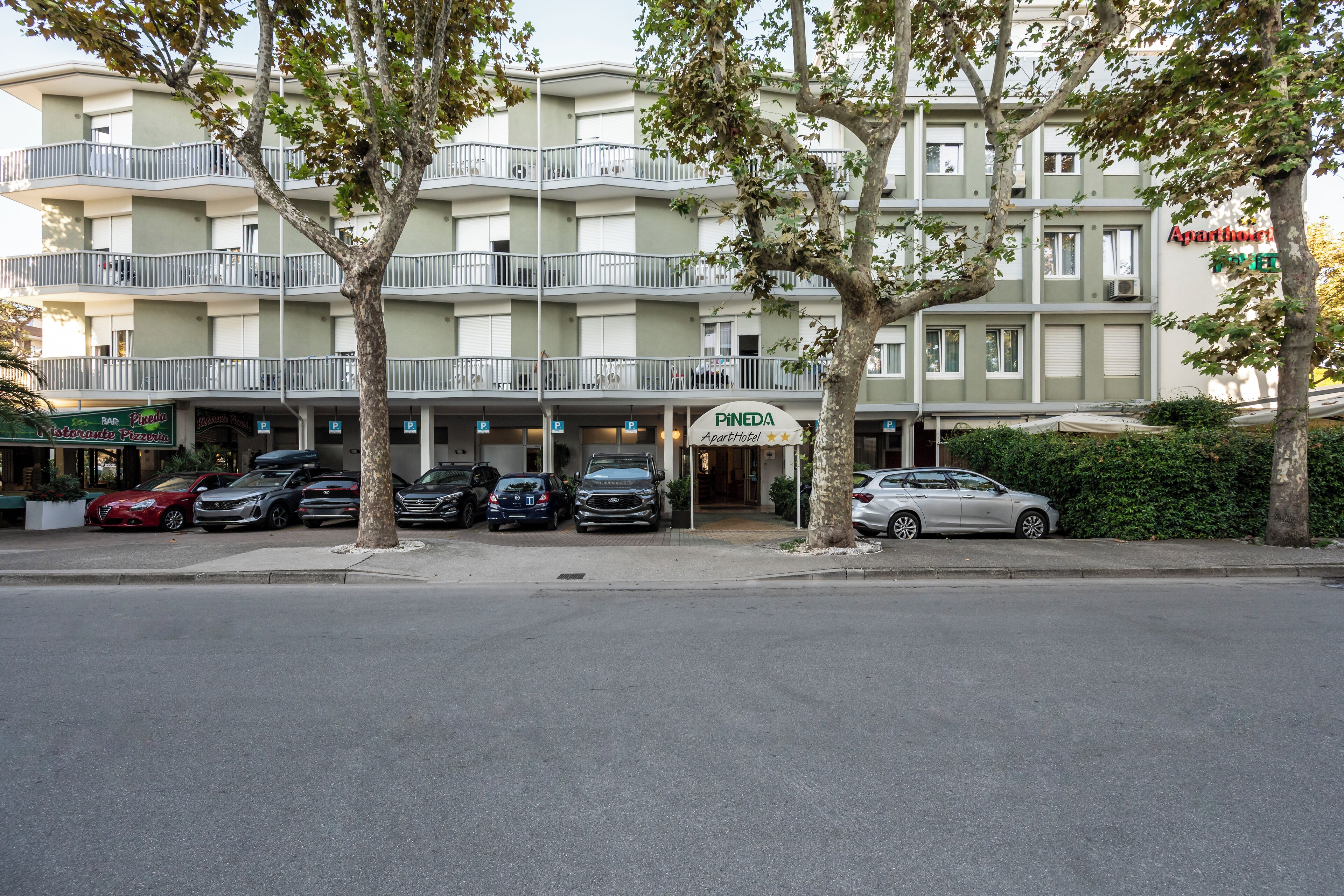 A multi-story building with balconies, a parking area, and a sign for 'Pineda Apartamentos'.