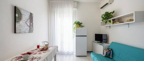 A compact living space with a dining area, a sofa, a TV, and a refrigerator.