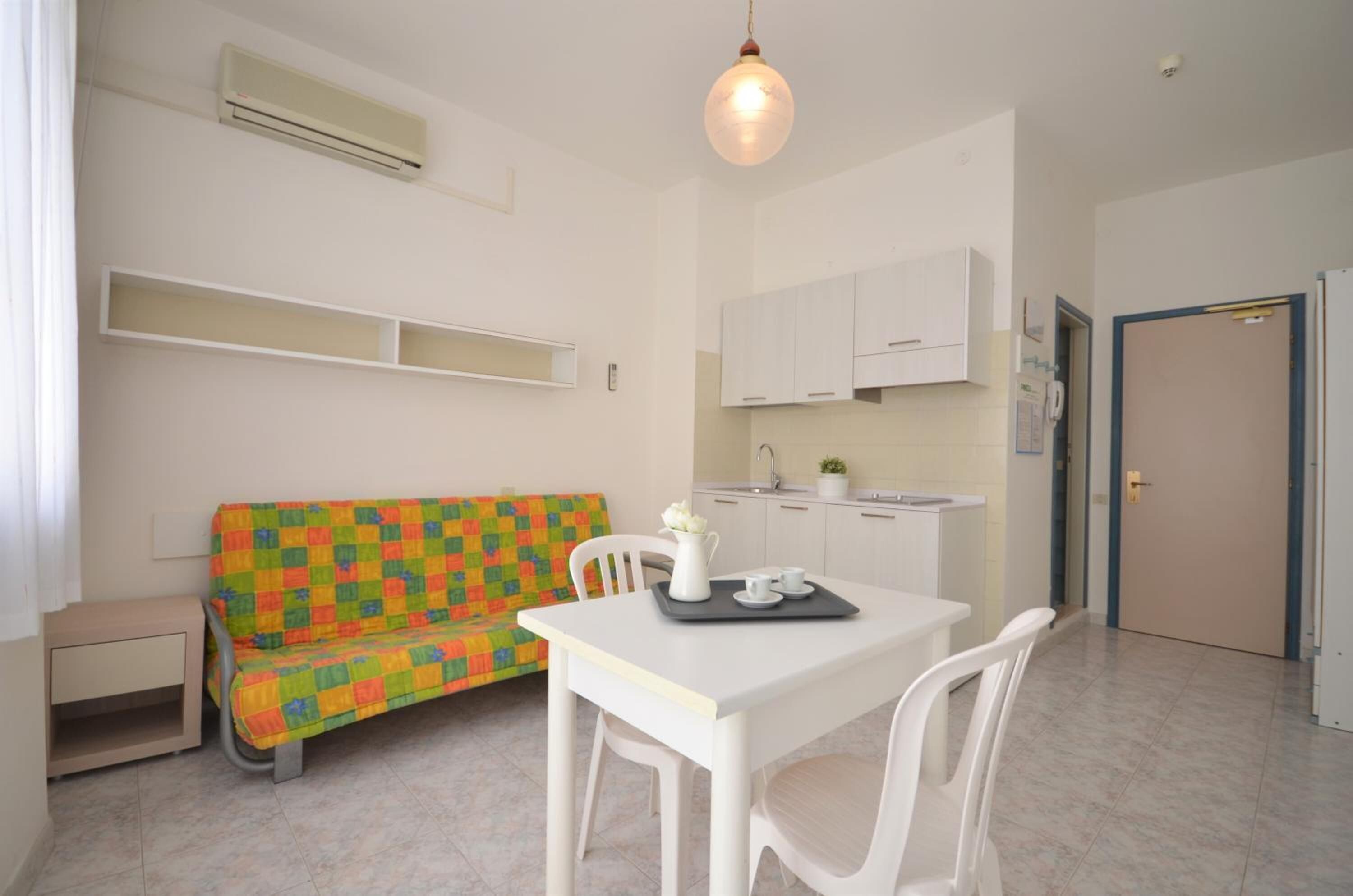 A small, bright room with a white sofa, a dining table, and a kitchen area.