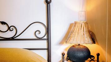 A bed with a yellow blanket, a black metal headboard, a small bedside table with a lamp, and a wall-mounted light fixture.