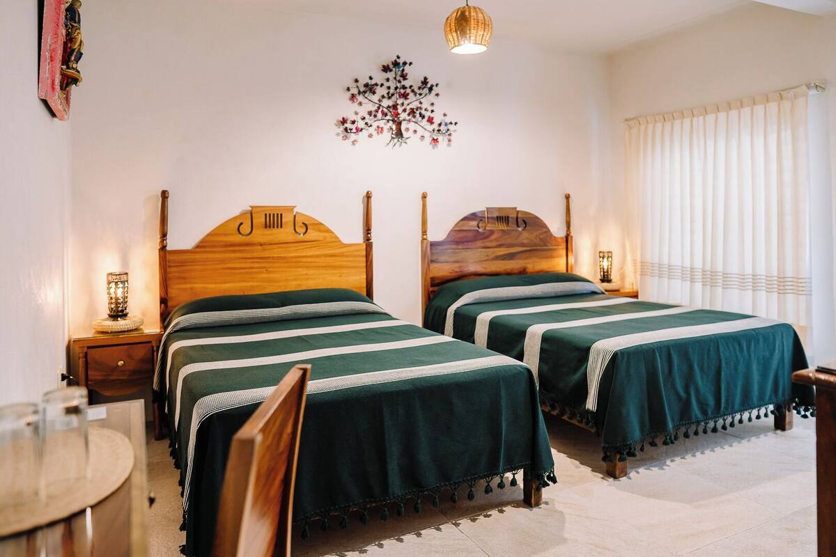 Una habitación de hotel con dos camas de madera, una mesa redonda y un adorno en la pared.