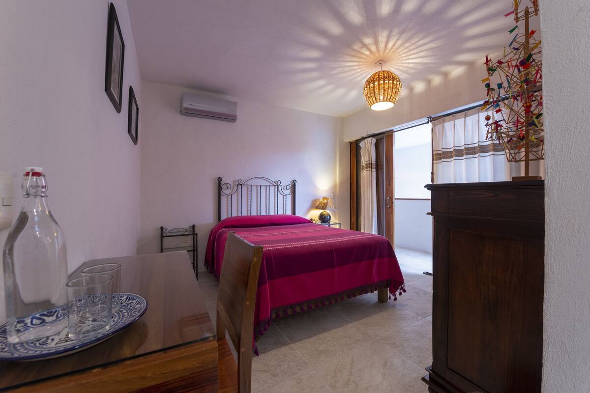 Un dormitorio con dos camas, una mesita de noche con una botella y vasos, una lámpara y una planta decorativa.