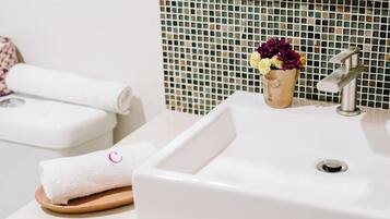 Un baño con lavamanos blanco, espejo y salpicadero de azulejos.
