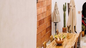 A dining area with a long wooden table, chairs, a cactus, and a brick wall. - La Casa Carlota (Oaxaca)