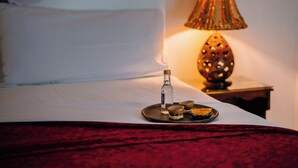A neatly made bed with a red blanket, a bedside table with a decorative lamp, and a tray with a bottle and bowls. - La Casa Carlota (Oaxaca)