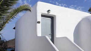 A white building with a door and a small window, surrounded by palm trees and a clear sky. - Albatros Club Mykonos (Mykonos)
