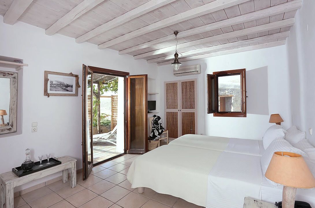 Quarto com cama, luminária de cabeceira, mesinha com bandeja, espelho e porta para área externa.