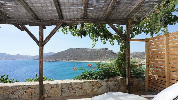 A covered outdoor seating area with a stone wall and a view of the sea and mountains. - Albatros Club Mykonos (Mykonos)